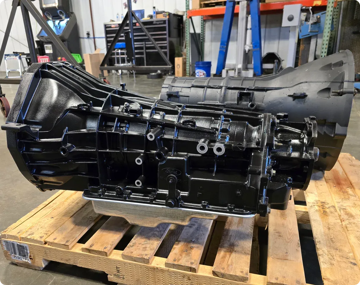 1023 Diesel & Fleet: A black transmission sits on a wooden pallet in an industrial setting. Shelves with equipment and tools are visible in the background.