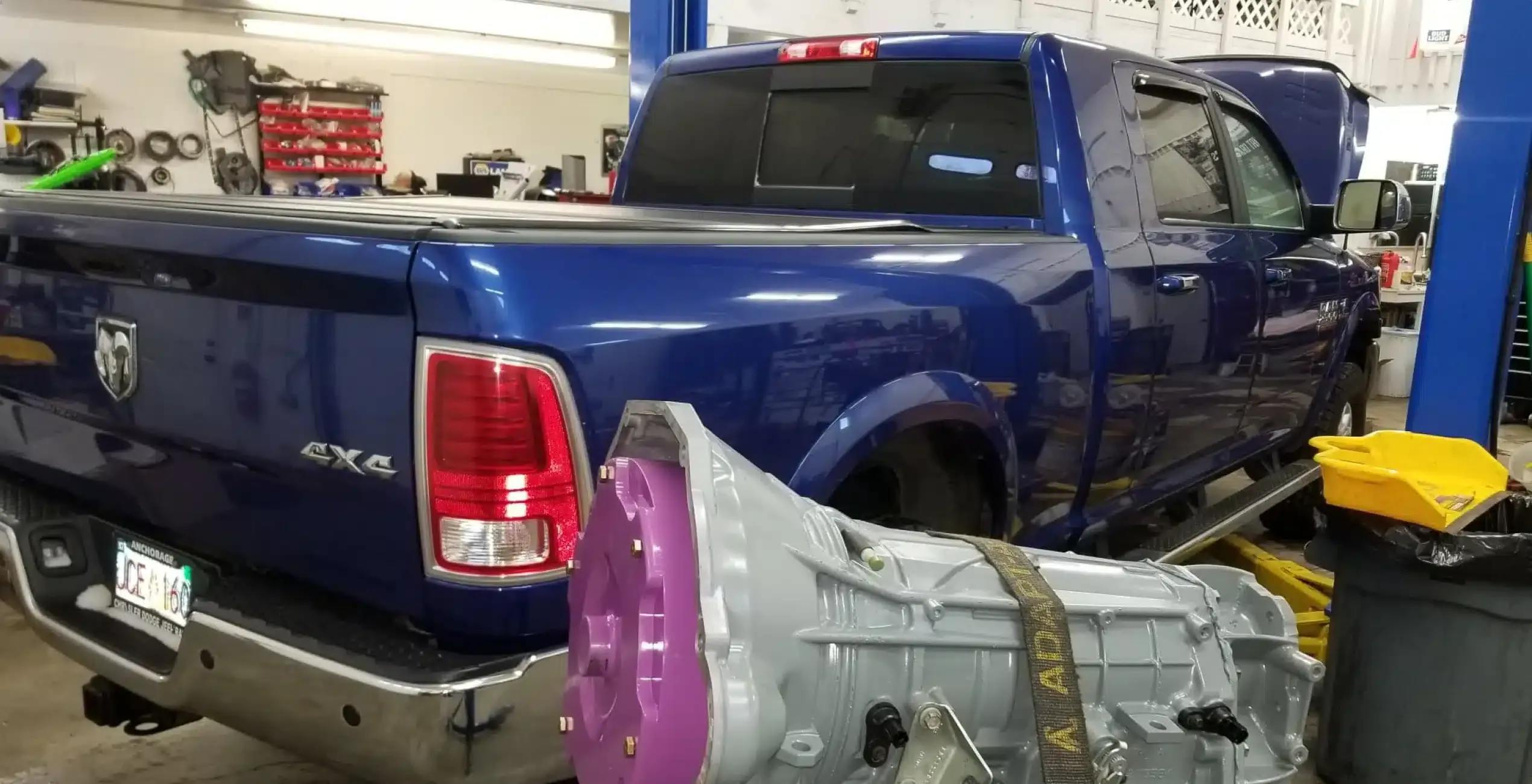 Cummins diesel repair in Palmer, AK at 1023 Diesel & Fleet: a blue pickup truck with its hood open in the shop, with a transmission resting on the floor in the foreground.