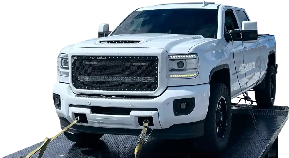 A white pickup truck with a large front grille secured on a flatbed trailer with straps.