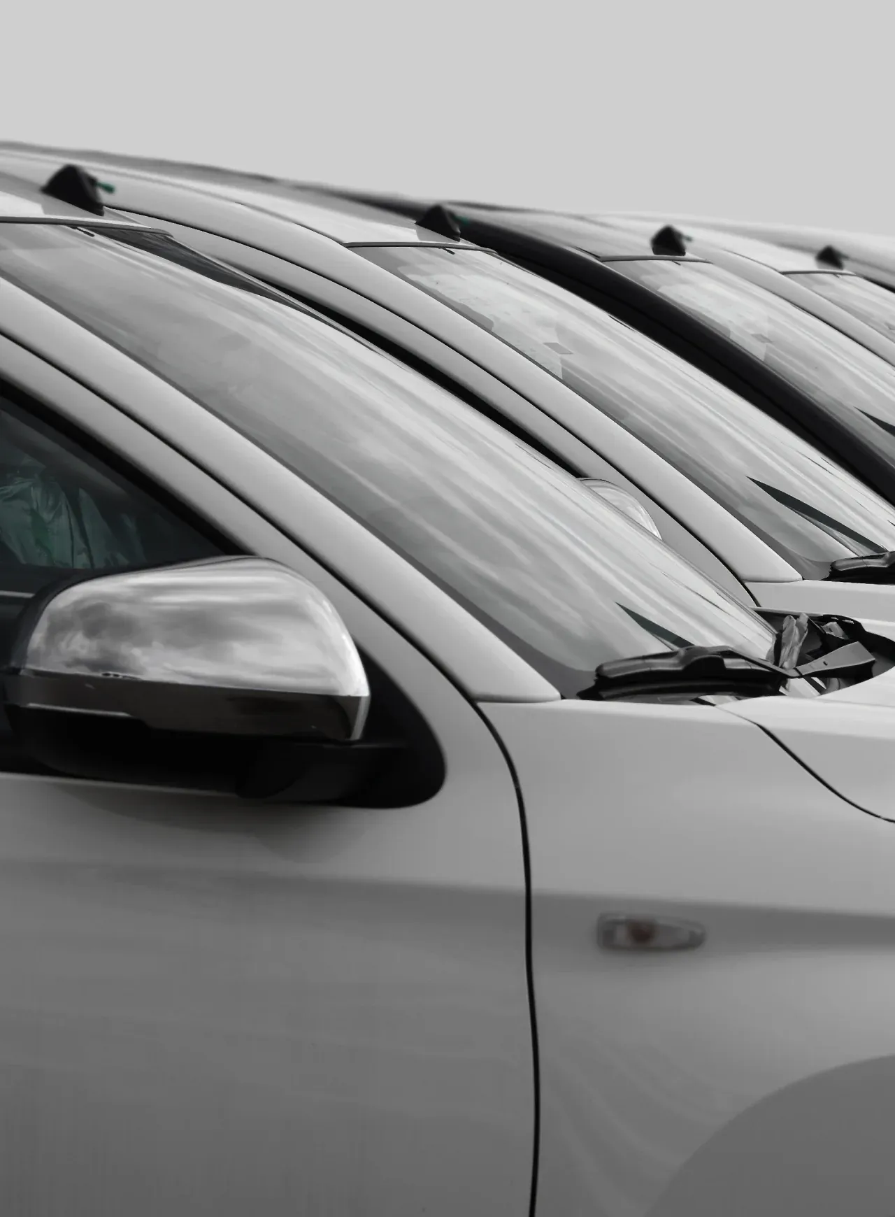 1023 Diesel & Fleet: A row of white cars parked closely together. The focus is on the side mirrors and windshields, highlighting the uniformity and alignment of the vehicles.