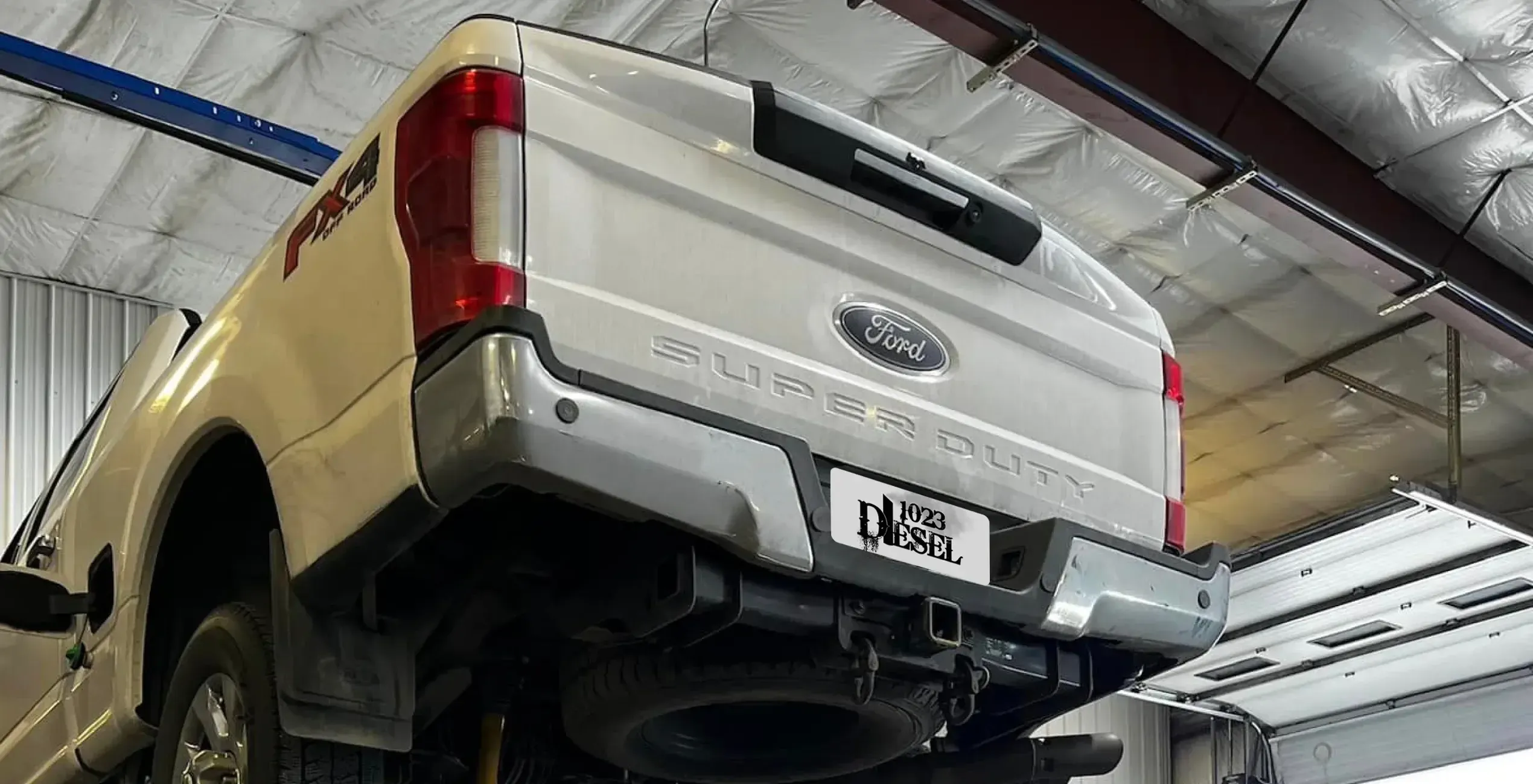 Powerstroke repair in Palmer, AK at 1023 Diesel & Fleet: a white Ford Super Duty truck lifted in the shop, seen from the rear.