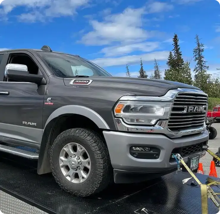 A gray Ram 2500 truck secured with straps on a platform under a partly cloudy sky