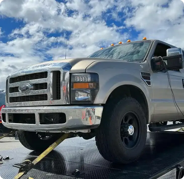 A silver Ford truck on a flatbed trailer under a partly cloudy sky