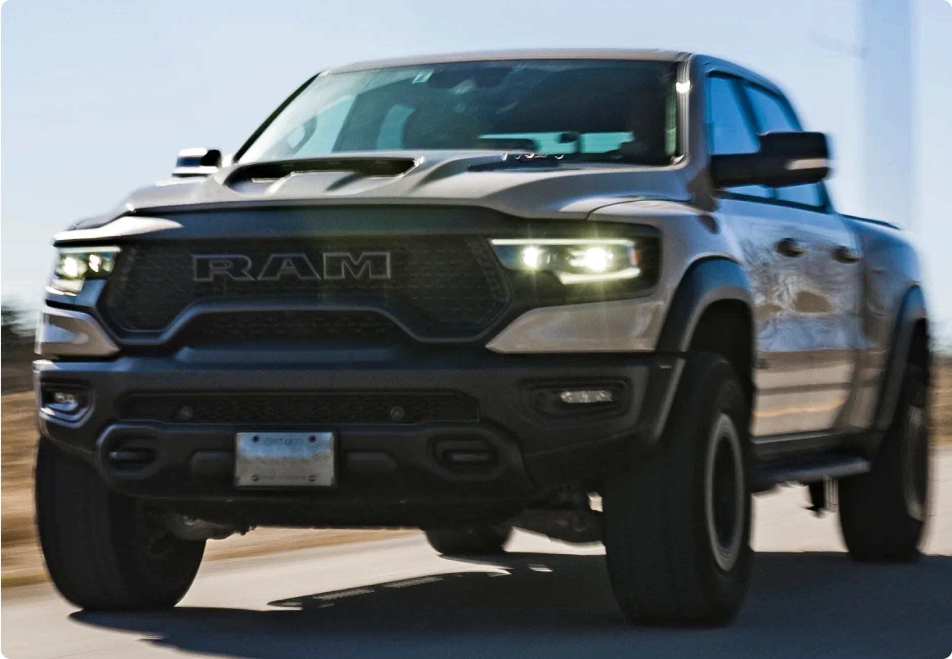 1023 Diesel & Fleet: a silver RAM pickup truck driving on a road with its headlights on, motion blur in the background.